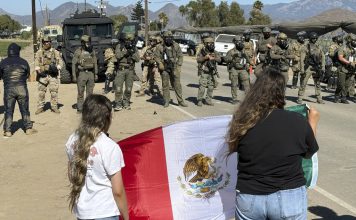 Demonstrators hold a flag in front of federal agents blocking a road during an immigration raid in Camarillo, Calif. (AP Photo/Michael Owen Baker)